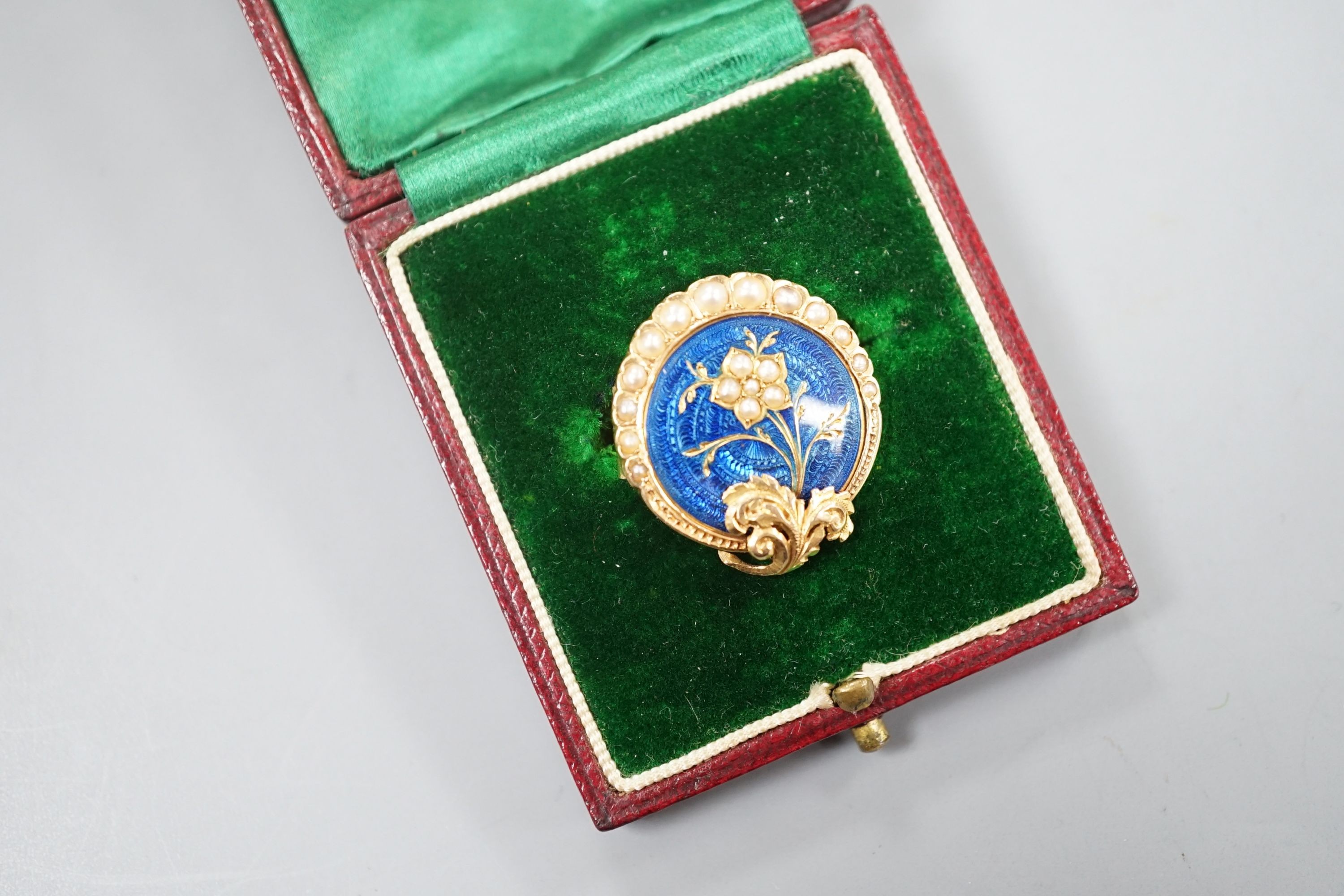 A nearly 20th century yellow metal, blue enamel and seed pearl set circular brooch, 22mm, gross 4.5 grams, in fitted box.